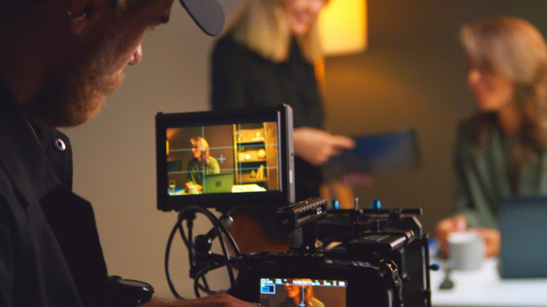 Filmmaker operates a professional camera with a monitor showing a seated person being filmed.