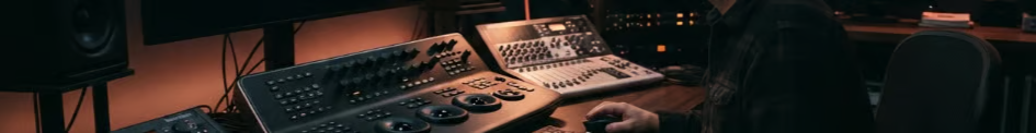 Audio engineer operating a large mixing console in a dimly lit recording studio.