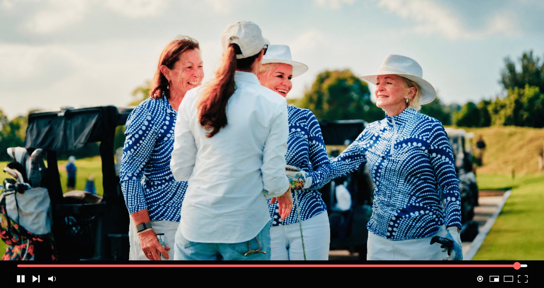 Four women in blue-and-white golf attire stand together on a sunny golf course.