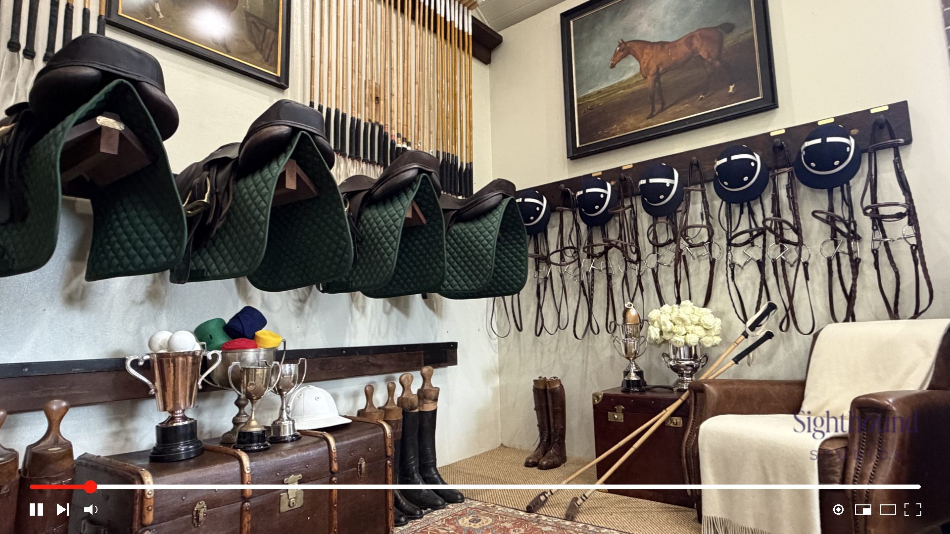 Equestrian tack room with saddles, bridles, helmets, trophies, boots, and horse artwork.