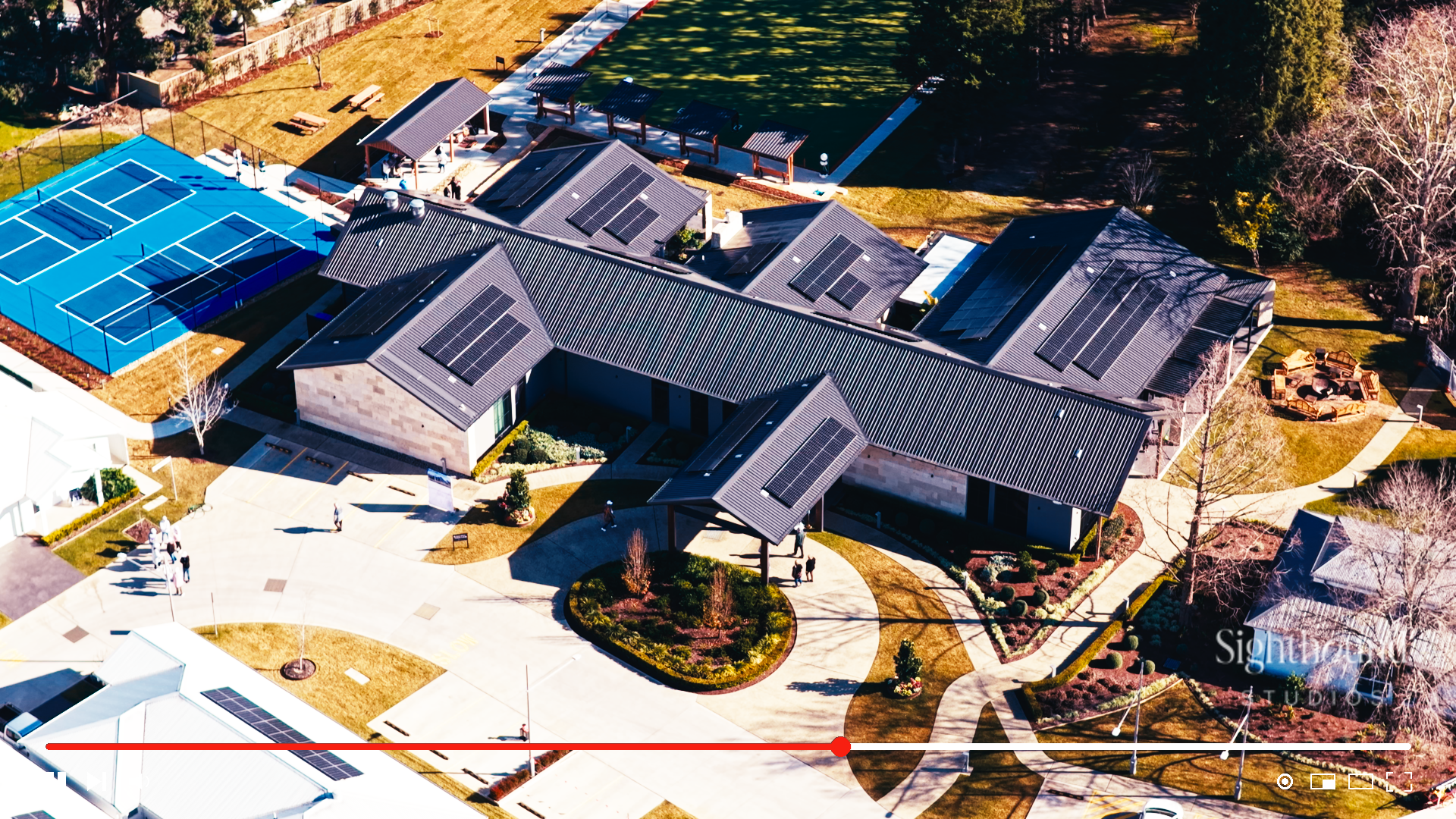 Aerial view of a solar-paneled recreation complex with blue tennis courts and landscaped paths.